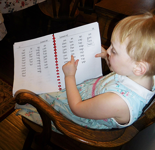 Child pointing out a word in her Alpha-Phonics workbook